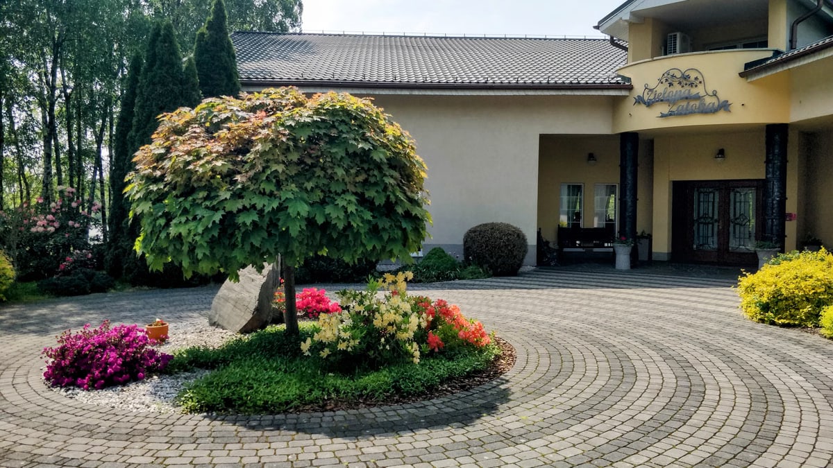 Beautiful inn entrance surrounded by lush gardens and colorful flowers on a sunny day.